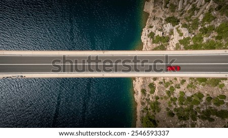 Top down view of a red car alone driving on a bridge over the sea. Background images for travel, holidays, the beauty of traveling by car to discover a country. Maslenica bridge, Croatia.