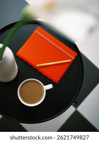 Top down view at red notebook with pen, mug of coffee and vase with flowers on a coffee table at home