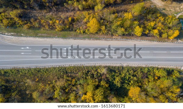Top down view of road with car in autumn forest at\
sunset. Amazing landscape with rural road, trees with orange leaves\
in day.