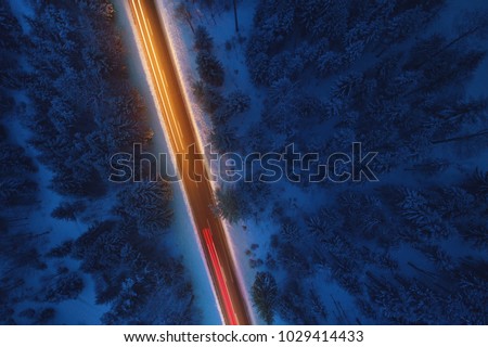 Top down view to road in the snowy wood. Romantic night aerial photo of cars traveling on the mountain road.