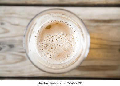 Top Down View Of The Round Mouth Of A Beer Glass With Foam And Bubbles On The Surface, With A Blurry Wood Table Background, At A Local Craft Brewery