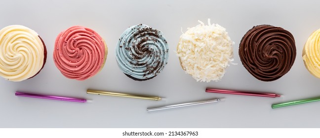 Top down view of a row of cupcakes with various toppings and candles below. - Powered by Shutterstock