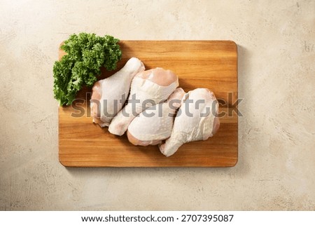 A top down view of several raw chicken drumsticks, on a wood board.