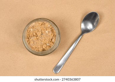 A top down view shows a small glass jar filled with carp roe with garlic next to a metal spoon on a brown paper surface.