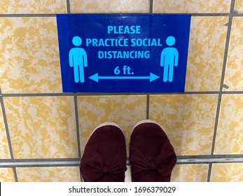 Top Down View Of A Sign In A Grocery Store Reminding Customers To Practice Social Distancing Due To Coronavirus COVID-19 Pandemic Outbreak In The United States. Feet Shown In Picture