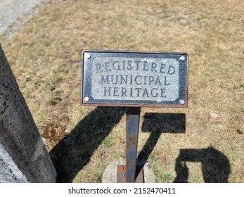 A Top Down View Of A Sign Saying Registered Municipal Heritage. The Sign Is Engraved In A Small, Metal, Rectangular Plaque.