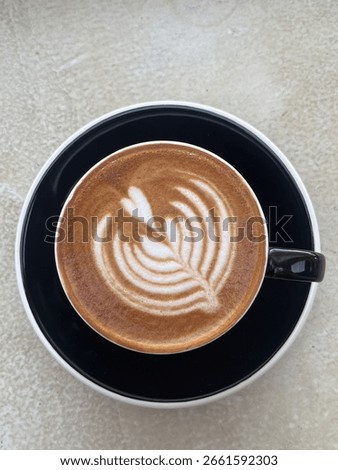Top down view of single cup of coffee with leaf latte art inside a black ceramic cup and white marble table in the background