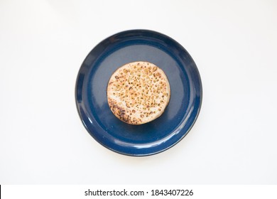 Top Down View Of A Single English Crumpet On A Plate Against A White Background. The Baked Breakfast Cake Is Full Of Holes.