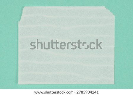 Top down view of a single white sheet of dissolvable laundry detergent paper isolated on a plain green background.