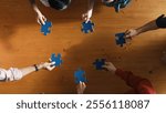 Top down view of skilled business people separated blue jigsaw puzzle on meeting table. Group of diverse team working together to solve the puzzle. Represented togetherness, cooperative. Convocation.