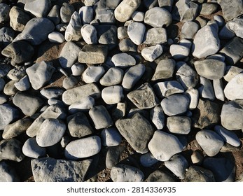 Top down view of smooth grey river stones and pebbles on a beach.