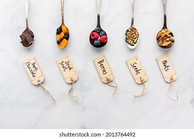 Top Down View Of Spoons Filled With Various Ingredients Used In Trail Mix And Smoothie Bowls With Wooden Labels.