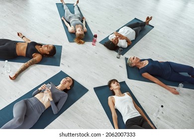 Top down view of sporty multiethnic women in sportswear relax lie on mats in fitness studio meditate after yoga practice. Active diverse multiracial female group have stretching mediation do sports.
