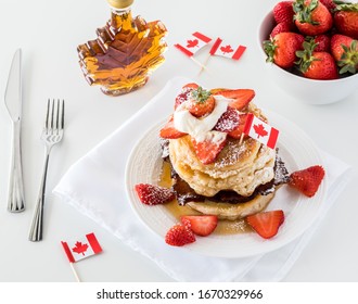 A Top Down View Of A Stack Of Pancakes With Strawberries For Canada Day And A Maple Leaf Shaped Bottle Of Syrup.