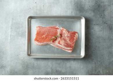 A top down view of a stack of raw bacon on a baking sheet.