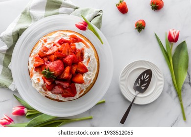 Top down view of a strawberry shortcake on a cake platter with serving dishes to the side.