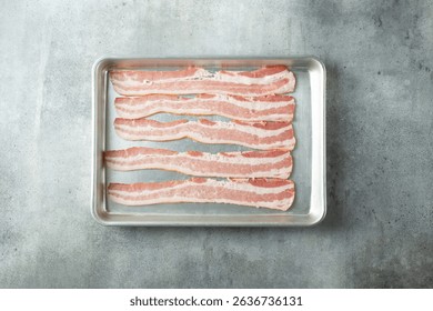 A top down view of strips of raw bacon on a baking sheet.