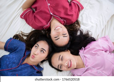 Top Down View Of Three Teenage Girls Smiling At The Camera While Lying Together On The Bed And Having Sleepover Party At Home