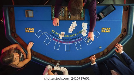 Top Down View Of Two Gamblers Playing Blackjack In Luxurious Casino. Dealer Distributing Cards To Anonymous Male And Female Caucasian Players, Who Make Bets, Moving Chips To Center Of Table.