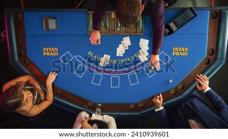 Top Down View Of Two Gamblers Playing Blackjack In Luxurious Casino. Dealer Distributing Cards To Anonymous Male And Female Caucasian Players, Who Make Bets, Moving Chips To Center Of Table.