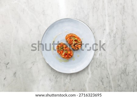 Top down view of two pieces of classic Italian bruschetta with chopped fresh tomatoes, basil, and olive oil drizzle served on a blue ceramic plate over a white marble table.
