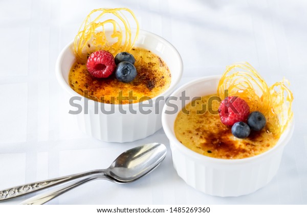 Top\
down view of two ramekins filled with creme brulee and topped with\
berries and spun sugar decorations ready for\
eating.