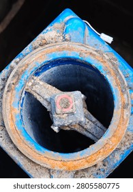 Top down view of an underground fire hydrant system with a blue cast iron housing and a rusty metal flange.