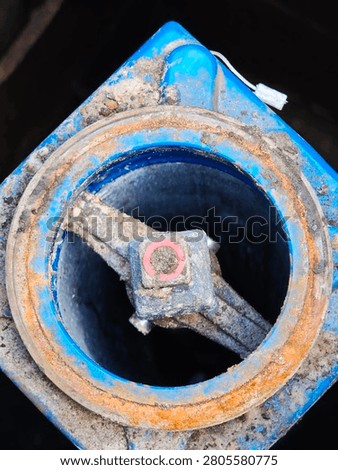 Top down view of an underground fire hydrant system with a blue cast iron housing and a rusty metal flange.