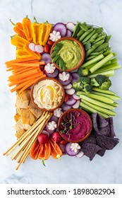 Top down view of a vegetable charcuterie platter with hummus dips against a light background.
