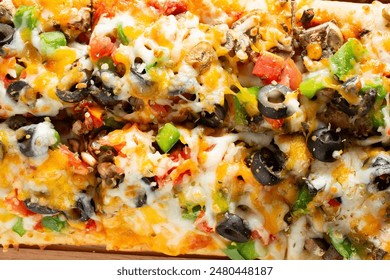 A top down view of a veggie flatbread, featuring toppings as black olives, bell peppers and cheese.