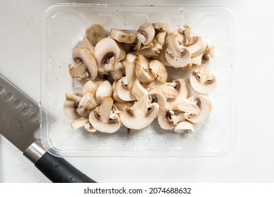 Top Down View Of Washed Sliced Mushrooms Against A White Background. A Knife Is On The Contertop. Cooking Or Meal Prep Concept.