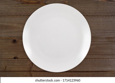 Top Down View Of A White Plate Sitting Expectantly On A Rustic Knotted Brown Wood Table Top. 