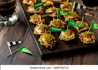 A Top Down View Of A Wooden Platter With Layered Dip Appetizers Ready For A Game Day Celebration.