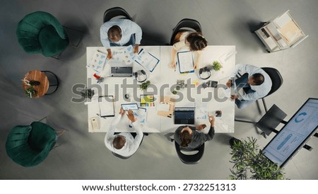 Top down view of work team in multinational company analyzing metrics and projections. Staff collaborates on strategy planning and report sharing to support business targets.