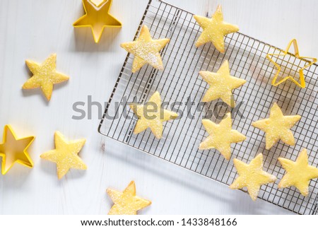 Top down view of yellow star shaped sugar cookies with yellow icing, sprinkles and powdered sugar ready for eating.