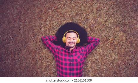 Top Down View Of Young Man Enjoying Music With Headset While Lying On The Grass At Park