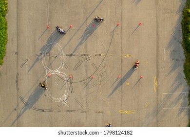 Top Down Wide Aerial View Of Four Riders Having Fun On An Advanced Motorcycle Training Slalom Course Between Orange Cones With Long Shadows, And Tire Marks 