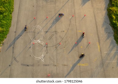  top down wide aerial view of four riders having fun on an advanced skill motorcycle training slalom course between orange cones with long shadows, painted lines and tire burnout marks 