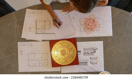 TOP DOWN: Young female analysing and making plan of feng shui for house building. Feng shui expert analysing energy flow distribution for balanced home and efficient house interior design arrangement. - Shutterstock ID 2184485739