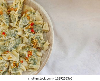 Top eye view closeup and blurred circle of Gyoza or dumplings filling minced pork, cabbage, and chives isolated on a white plate, with chili, garlic, and soy sauce, on white fabric table, chopsticks