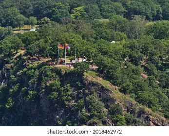 Top of famous slate rock Loreley (Lorelei) above Rhine river with flying flags of Germany and Rhineland-Palatinate on sunny summer day with tourists enjoying the view from the platform.