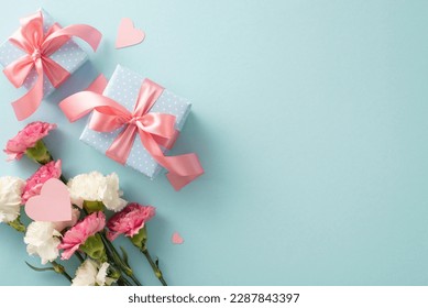 Top flat lay photo of beautiful present boxes with pink ribbon, carnation flowers with pink paper hearts on pastel blue background with empty space for text or advert
