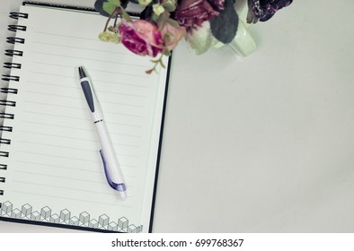 Top or flat lay view of eyeglass and notebook with flower decoration on white table background with copy space.