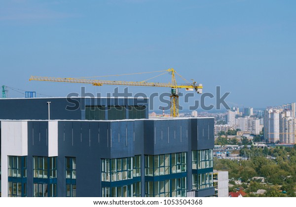 Top floor\
of  building construction. Construction site with yellow crane and\
building. Crane and building construction site against blue sky and\
city districts in the\
background.