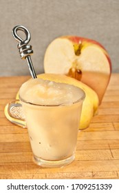 Top, Front View, Close Distance Of A Glass Cup Filled With Apple Sauce, With Artisan Spoon And A Halved Ambrsa Apple, Exposing Interior, Seed, On Maple Wood Cutting Board