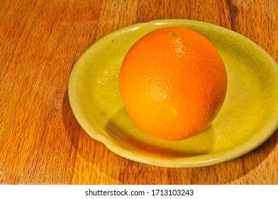 Top, Front View, Medium Distance Of, A Freshly Picked, Ripe, Local, Orange, On A Yellow-green Plate, On A Maple Wood Cutting Board