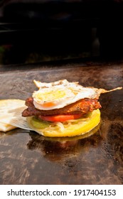 top, front view, medium distance of a Italian sausage, lettuce, tomato, cheese sandwitch cooking on a flat top grill, at a tropical farers market