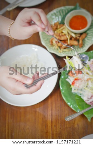Top of hands holding fork and spoon and eating thai food on dinning table at restaurant in flat lay food concept.Close up.