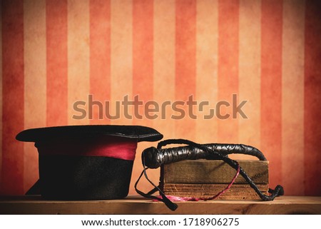 A top hat and whip, tools of a lion tamer. With a circus or carnival style stripe background.