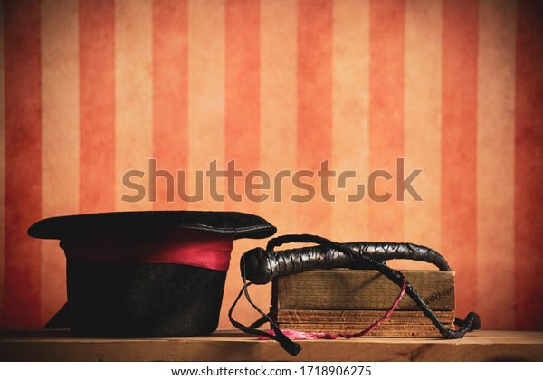 A top hat and whip, tools of a\
lion tamer. With a circus or carnival style stripe\
background.